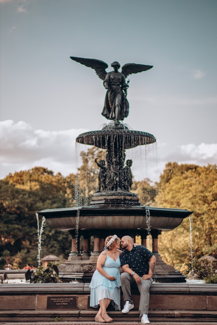 newly wed couple in Manhattan, New York, sitting by bethesda fountain in central park, kissing, while the mom is expecting holding her belly in a baby blue dress. 