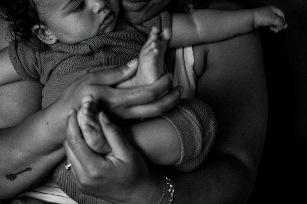 close up black and white photograph of a mother holding her infant, while appreciating her daughters tiny toes