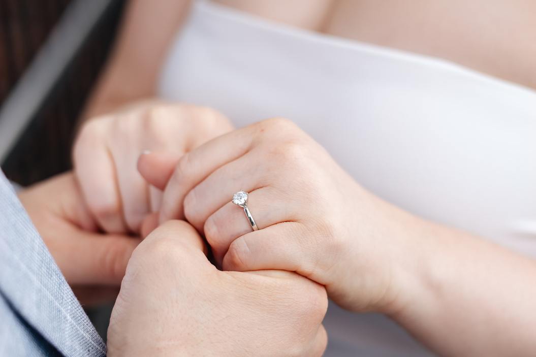 close up of engagement ring while newly engaged couple hold hands