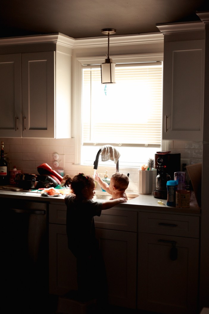 big sister helps mommy bathe little sister in the. kitchen sink