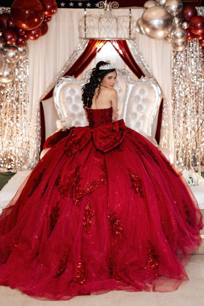 Quinceañera dressed in a red ball gown during her celebration at a VFW hall in Stratford, Connecticut, surrounded by elegant decor and traditional seating as she celebrates her fifteenth birthday, photographed in a documentary style to capture an authentic milestone event