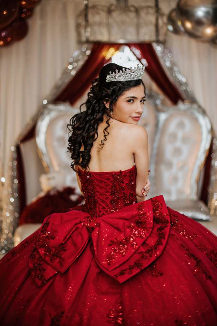 Quinceañera dressed in a red ball gown during her celebration at a VFW hall in Stratford, Connecticut, surrounded by elegant decor and traditional seating as she celebrates her fifteenth birthday, photographed in a documentary style to capture an authentic milestone event.