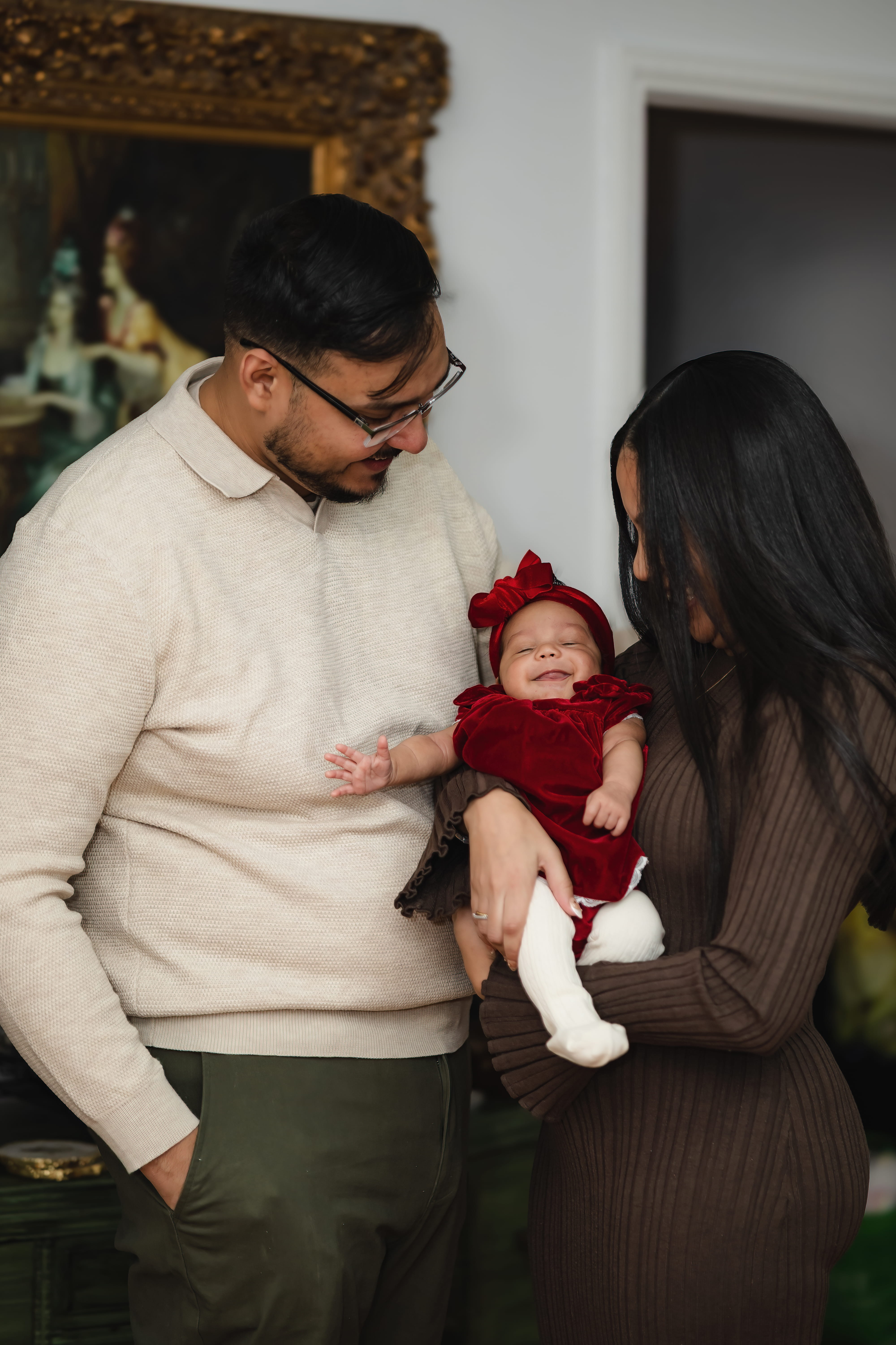 Dad holding newborn baby girl in red outfit during intimate family session in Queens NY.