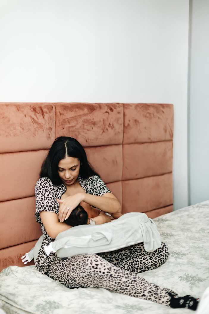 Mother holding newborn baby girl near nursery wall during candid in home documentary session.